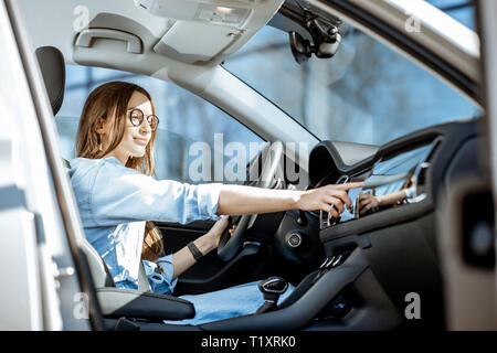 Junge Frau berühren Auto überwachen, während in der modernen Autos in der Stadt sitzen Stockfoto