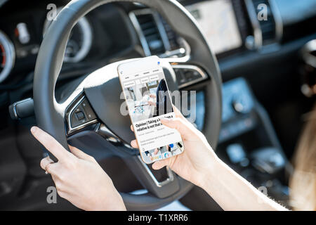 Frau liest finanzielle Nachrichten auf dem Smartphone während der Fahrt Auto, Nahaufnahme Stockfoto