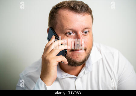 Überrascht Männchen in weißen T-Shirt ist das Telefonieren auf einem weißen Hintergrund grau Stockfoto