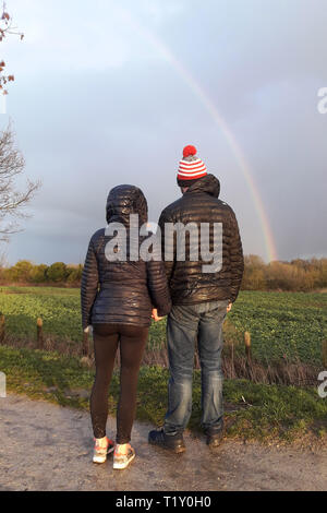 Ein Paar aus ihren Hund halten Hände wandern und bis auf einen Regenbogen in Warwick, Warwickshire. März 12, 2019. Stockfoto