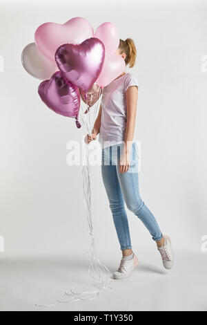 Mädchen in legere Kleidung, Gesicht mit herzförmigen rosa Luftballons auf Weiß Stockfoto