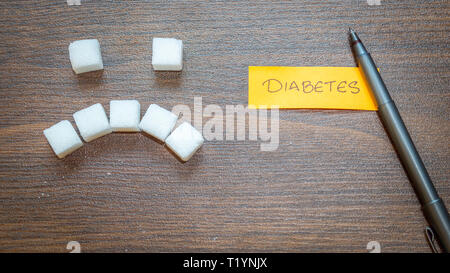 Diabetes Inschrift. Würfel Zucker mit einem traurigen Lächeln Gesicht auf einem hölzernen Hintergrund. Stockfoto