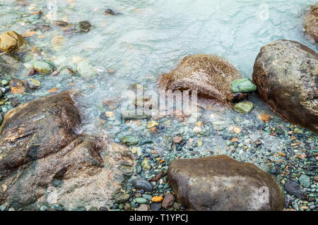 Felsbrocken und Steine am Ufer eines Flusses mit milchig Grün Wasser Stockfoto