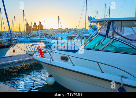 Der Blick von der Marina auf die Silhouetten der Yachten Segel und Msida Pfarrkirche in den letzten Sonnenuntergang Strahlen, Malta. Stockfoto