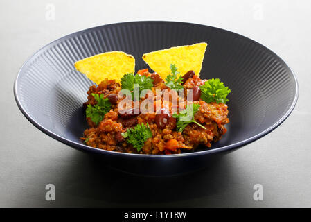 Chili con carne Essen in einem rustikalen Schüssel. Traditionelle Gericht der mexikanischen Küche mit Bohnen, Hackfleisch, Petersilie und Tortilla Chips Stockfoto