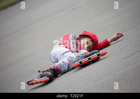 Der Junge im Rollschuhe liegen auf dem Bürgersteig. Das Kind in Rollschuhen fiel Stockfoto