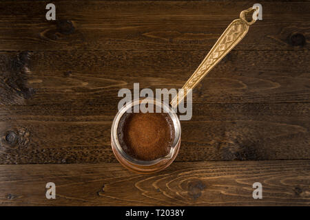 Braun alte Kupfer cezve mit Kaffee. Über braunes Holz Tabelle als Hintergrund. Mit Kopie Raum auf der linken Seite. Ansicht von oben. Stockfoto