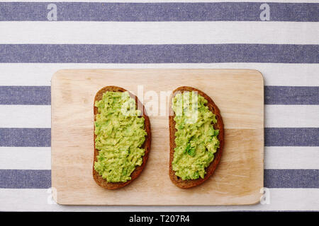 Guacamole Sandwich auf hellen Hintergrund avocado Sandwiches auf Holzbrett und textile Draufsicht Stockfoto