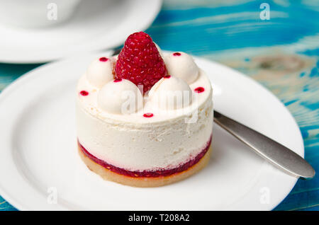 Weiß luftig-Torte mit Himbeeren Layer und Himbeere berry liegt auf eine weiße, runde Platte neben einem weißen Schale, die auf einem blauen Holztisch steht Stockfoto