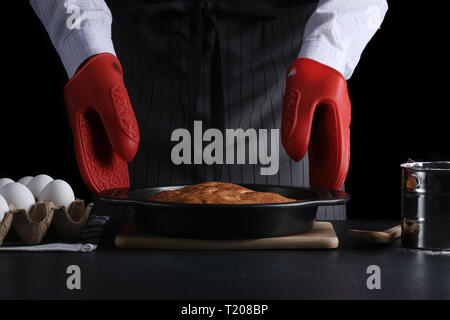 Mann in Schürze Holding frisch gebackene Torte auf dunklem Hintergrund. Rezept od-Torte oder Kuchen. Stockfoto
