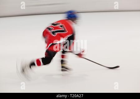 Jungen Hockeyspieler im roten Kleid mit Nummer 27 in Bewegung, verschwommene Bewegung auf dem Eis Stadion Stockfoto