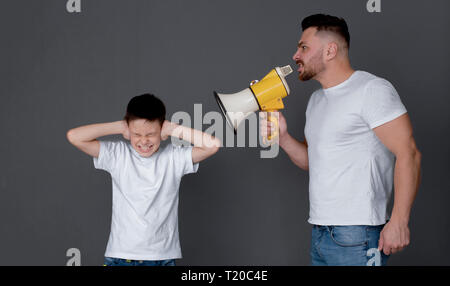 Probleme in der Familie. Wütende Vater mit Megafon schrie Sohn, der schließen Ohren und schielen, dunklen Studio Hintergrund Stockfoto