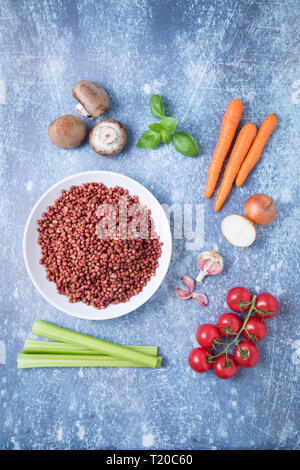 Red adzuki Bohnen in einer weißen Schüssel mit Wurzelgemüse. Pflanzliche Inhaltsstoffe auf grauem Hintergrund. Adzuki Abendessen Vorbereitung. Stockfoto