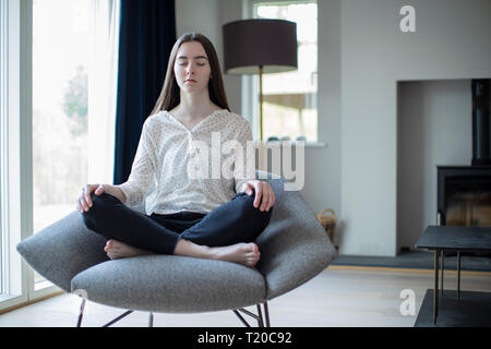 Friedliche Jugendmädchen Meditieren sitzt im Sessel zu Hause Stockfoto