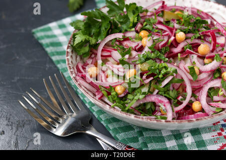 Gesunde Salate mit Kichererbsen, Kartoffeln, roten Zwiebeln und Gewürzgurken in einer Platte gegen einen dunklen Hintergrund Stockfoto