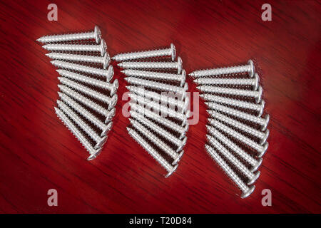 Drei Gruppen von silbernen Schrauben in den Zeilen auf einer Oberfläche mit Holz-finish angeordnet Stockfoto