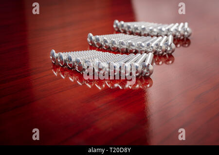 Drei Gruppen von silbernen Schrauben in den Zeilen auf einer Oberfläche mit Holz-finish angeordnet Stockfoto