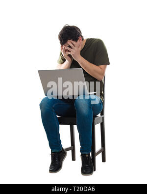 Lässige junge Mann sitzt auf Stuhl mit Laptop auf den Knien, Angst versteckt sein Gesicht mit Palm, auf dem Bildschirm durch die Finger. Frighte Stockfoto
