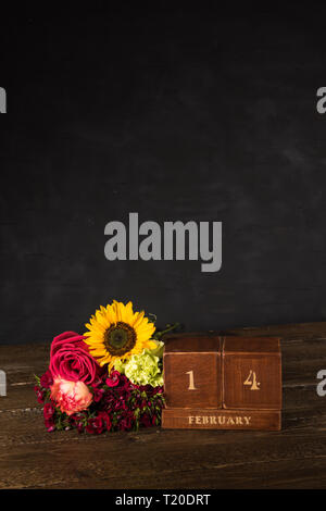 Happy Valentine's Day vintage Holz- Ewiger Kalender für Februar 14 auf einem schwarzen Hintergrund und eine Reihe von verschiedenen Blumen Stockfoto