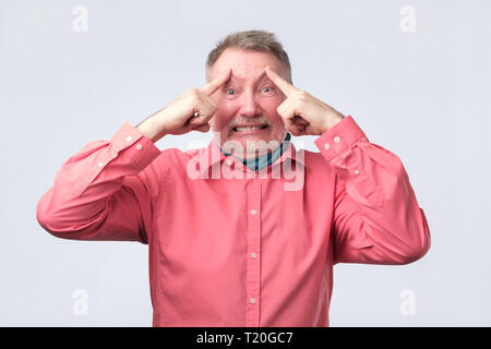 Reifen europäischen Mann im roten Hemd hält Finger auf Tempel und versuchte, an etwas zu erinnern. Versuchen Sie Idee zu generieren, Termin Konzept. Stockfoto