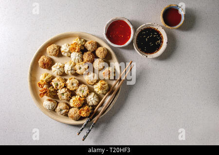 Dim Sum Gyozas asiatische gebratene Knödel Party mit verschiedenen Soßen in Keramik Teller serviert und Schüsseln mit Stäbchen über Grau gefleckten Hintergrund. Stockfoto