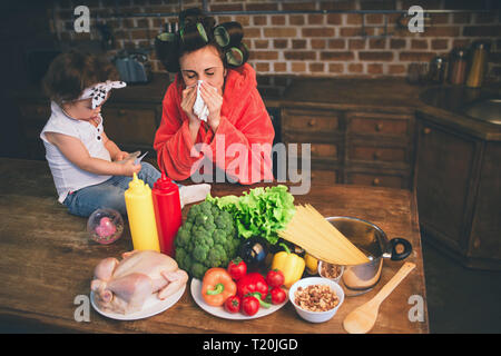 Betont Mama zu Hause. Junge Mutter mit Kind in der Küche zu Hause. Frau tun viele Aufgaben und kümmert sich um Ihr Baby. Die Frau ist krank und Sie Stockfoto