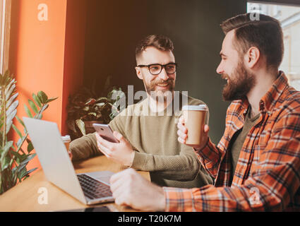 Schnittansicht der Kerle sitzen und in ein Gespräch. Auf von Ihnen ist dranking Kaffee, während andere ihm etwas erklärt und halten ein Telefon Stockfoto