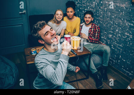 Nahaufnahme von einem Kerl, der singt ein Lied. Er versucht, es zu tun das Beste, wie er kann. Aber er ist fast Schreien ein Lied. Aber hir Freunde hören Stockfoto