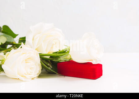 Blumenstrauß aus den weißen Rosen mit roten Geschenk Schmuck Kasten auf weiße Textur Hintergrund mit kopieren. 8. März, Valentines Tag oder Womans Tag Konzept Stockfoto