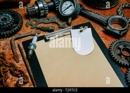 Teil von closeup Zwischenablage mit Papier und Label. Rostige Werkzeuge, Zahnräder um Banner auf vintage Metall Hintergrund. Motorrad Ausrüstung und Reparatur. Stockfoto
