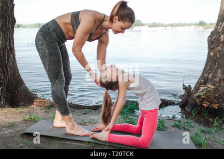 Schönes Bild von kleinen Mädchen nach hinten strecken. Sie hält ihre Füße mit Händen. Junge Frau hilft, ihre Bewegung zu tun. Sie sind stretc Stockfoto