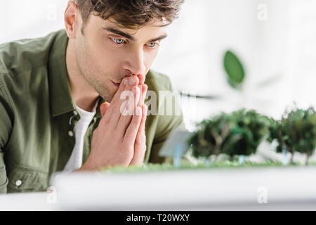 Selektiver Fokus der stattlichen Architect bei Tisch sitzen, Denken und auf der Suche nach Bäumen Modelle auf Gras im Büro Stockfoto