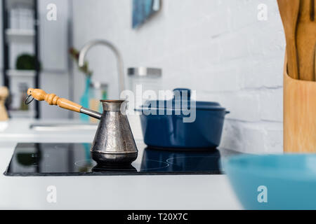 Selektiver Fokus der türkischen Metall cezve mit Griff am Ofen in der Küche Stockfoto
