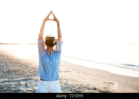 Blonde Frau tun Art von Yoga Übungen auf einem Strand in Thailand mit 3D Virtual Reality goggles Stockfoto