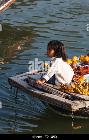 Nahaufnahme des kleinen Mädchens am Bug des Bootes mit produzieren Rubrik zu Hafen Markt in Halong Bay, Vietnam gefüllt sitzend Stockfoto