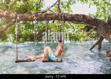 Mexiko, Yucatan, Quintana Roo, Lagune von Bacalar, Mann sitzt auf Baum schwingen über dem Wasser Stockfoto