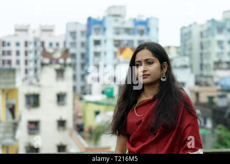 Schönen indischen Bengali Dame in rot glühenden Sari steht auf dem Dach mit der urbanen Landschaft als Hintergrund Stockfoto