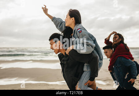 Zwei junge Männer, die ihre Freundinnen piggyback Rides am Strand. Fröhlicher junger Freunde genießen am Strand. Stockfoto