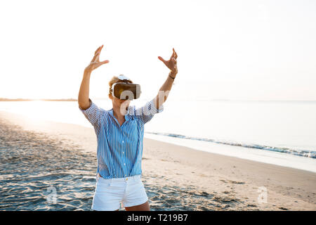 Blonde Frau tun Art von Yoga Übungen auf einem Strand in Thailand mit 3D Virtual Reality goggles Stockfoto