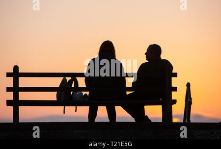 Borth, Aberystwyth, Wales. 29. Mär 2019. UK Wetter: Sonnenuntergang in Borth, Seebad Dorf an der Küste nördlich von Aberystwyth, Ceredigion, Wales, Großbritannien Sittingon Sitzbank entlang der Promenade an einem sonnigen Tag. Credit: Paul Quayle/Alamy leben Nachrichten Stockfoto