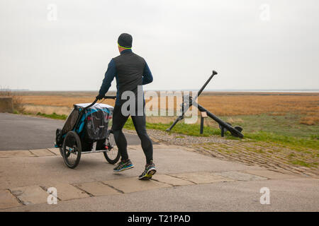 Einzelperson, Vater Rollen Kinderwagen Baby carraige Kinderwagen in Lytham Saint Annes, Lancashire. März 2019. Wetter in Großbritannien. Helle Outfits an einem trüben bewölkten Tag. Stockfoto