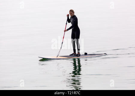 Branksome Dene, Poole, Dorset, Großbritannien. 30 Mär, 2019. UK Wetter: Diesig morgen Sonnenschein und kühler von spät, aber hört nicht auf Besucher Position am Meer in Branksome Dene. Frau paddleboarding. standup paddleboarder Standup Paddle boarder Credit: Carolyn Jenkins/Alamy leben Nachrichten Stockfoto