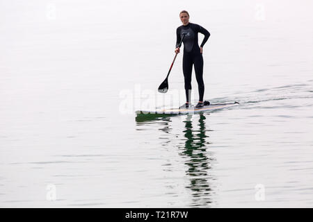 Branksome Dene, Poole, Dorset, Großbritannien. 30 Mär, 2019. UK Wetter: Diesig morgen Sonnenschein und kühler von spät, aber hört nicht auf Besucher Position am Meer in Branksome Dene. Frau paddleboarding. standup paddleboarder Standup Paddle boarder Credit: Carolyn Jenkins/Alamy leben Nachrichten Stockfoto