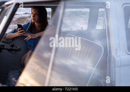 Frau mit Handy im Wohnmobil am Strand Stockfoto