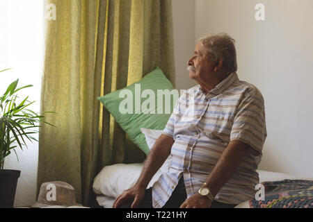 Ältere Menschen außerhalb des Fensters, während allein am Pflegeheim sitzen auf der Suche Stockfoto