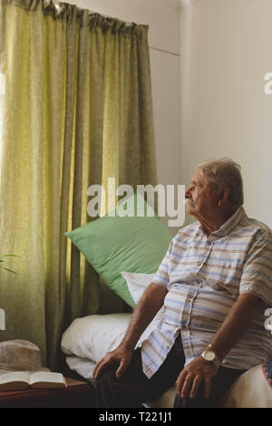 Ältere Menschen außerhalb des Fensters, während allein am Pflegeheim sitzen auf der Suche Stockfoto