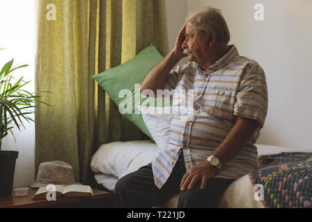 Ältere Menschen außerhalb des Fensters, während allein am Pflegeheim sitzen auf der Suche Stockfoto