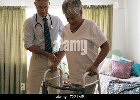 Männlicher Arzt helfen älteren weiblichen Patienten mit Walker zu gehen Stockfoto