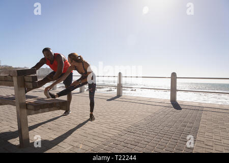 Junges Paar zu tun stretching Übung auf der Bank in der Nähe von Strand Stockfoto