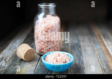 Rosa Himalaya Salzkristalle in der Glasflasche und kleine Schüssel auf Holztisch. Stockfoto